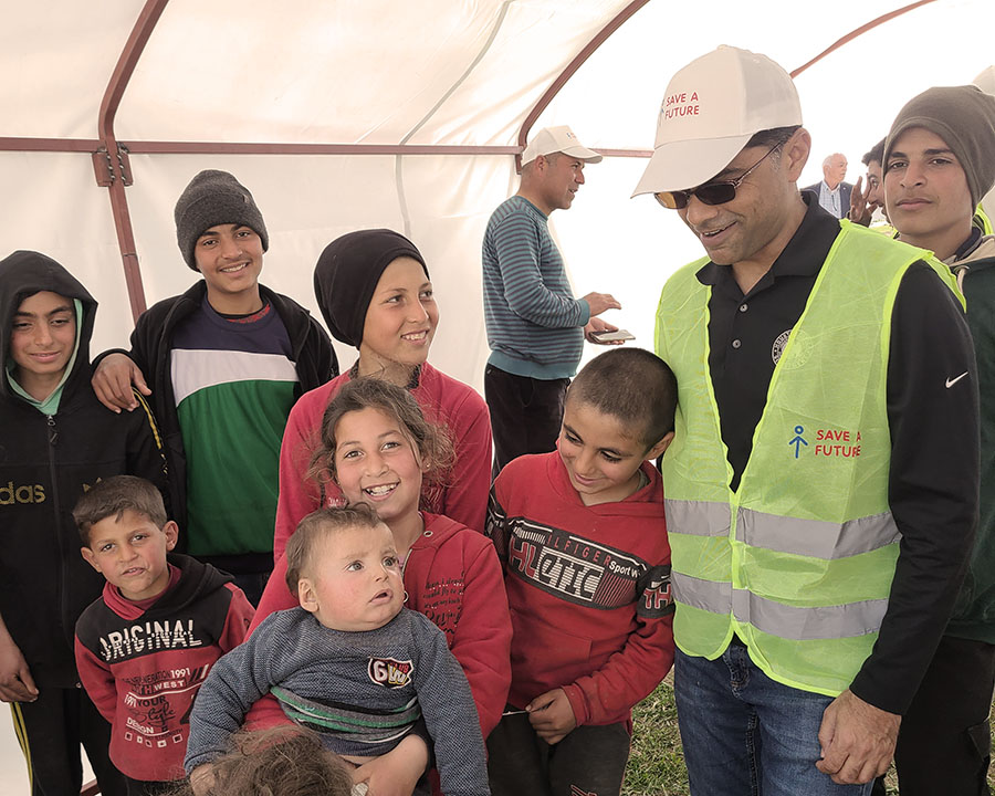 Man in green vest surrounded by ethnic children under a relief tent in Turkey.