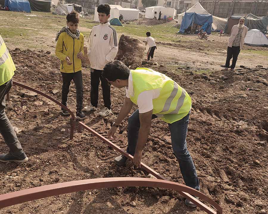 Men holding a steel structure to install tents for families displaced by earthquake in a region in Turkey.